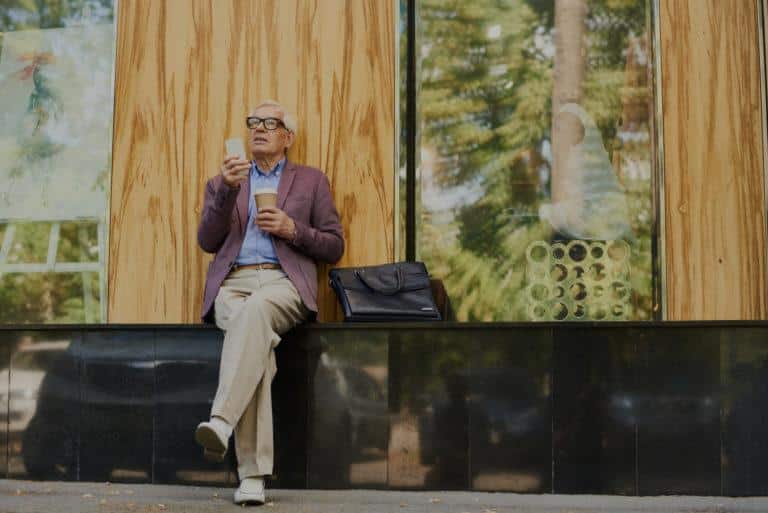 artheriopathie Homme assit dans la rue, regardant son téléphone et tenant un café