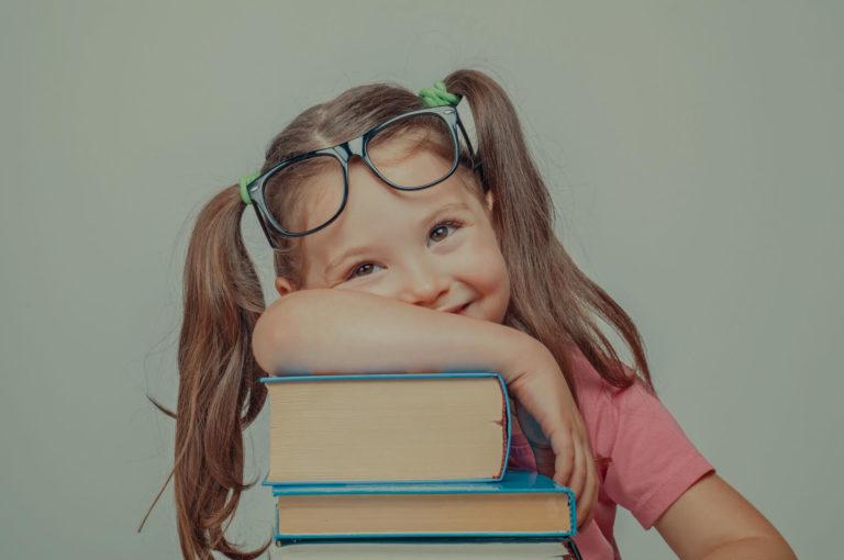 apprentissage par hypnose Petite fille portant des lunettes qui est accoudée sur une pile de livre