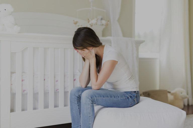 depression post partum Jeune maman qui se tient la tête, assise dans la chambre de son nouveau né
