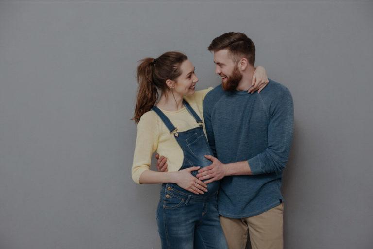 devenir papa Homme heureux regardant sa femme et posant ses mains sur le ventre de sa femme enceinte