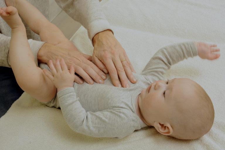 ostheopathie pediatrique Bébé calme, allongé sur un lit qui se fait masser le ventre