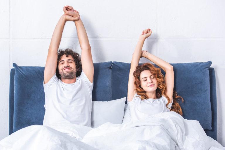 sommeil vacances Couple d'homme et de femme assis dans leur lit et s'étirant les bras