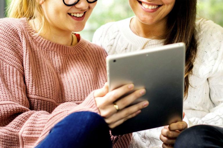teleconsultation-medicale-remboursement Deux jeunes femmes qui sourient en regardant un iPad