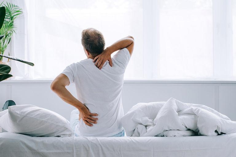soulager un mal de dos homme vue de dos qui s'étire assis dans sont lit